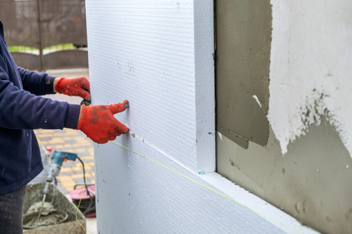 Construction worker installing styrofoam insulation sheets on house facade wall for thermal protection