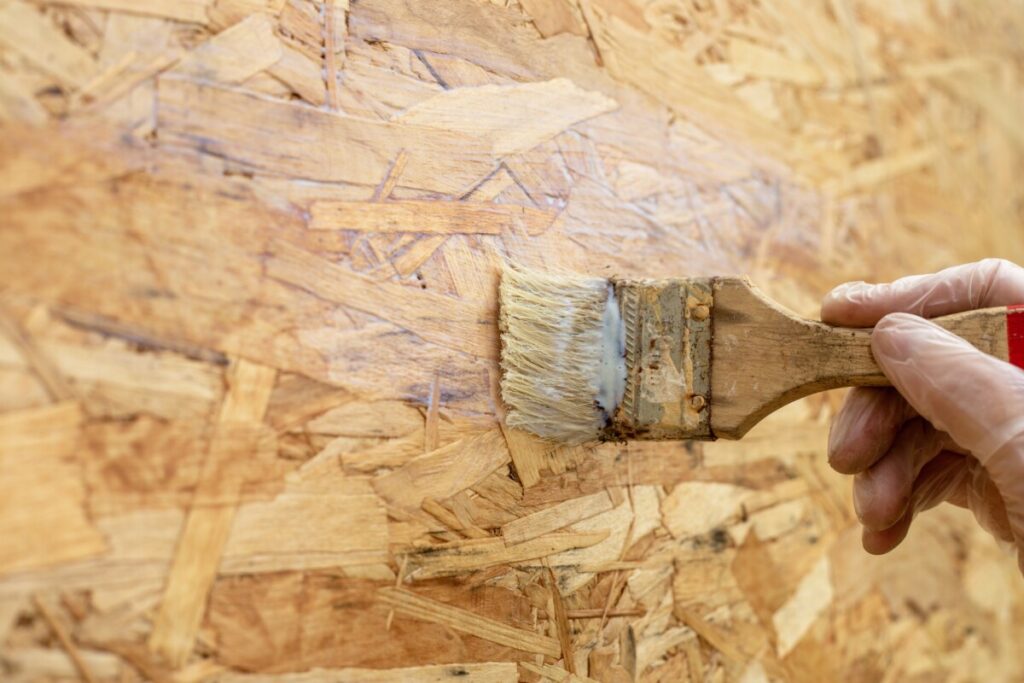 a female hand in a protective glove covers the OSB surface with acrylic varnish using a paint brush