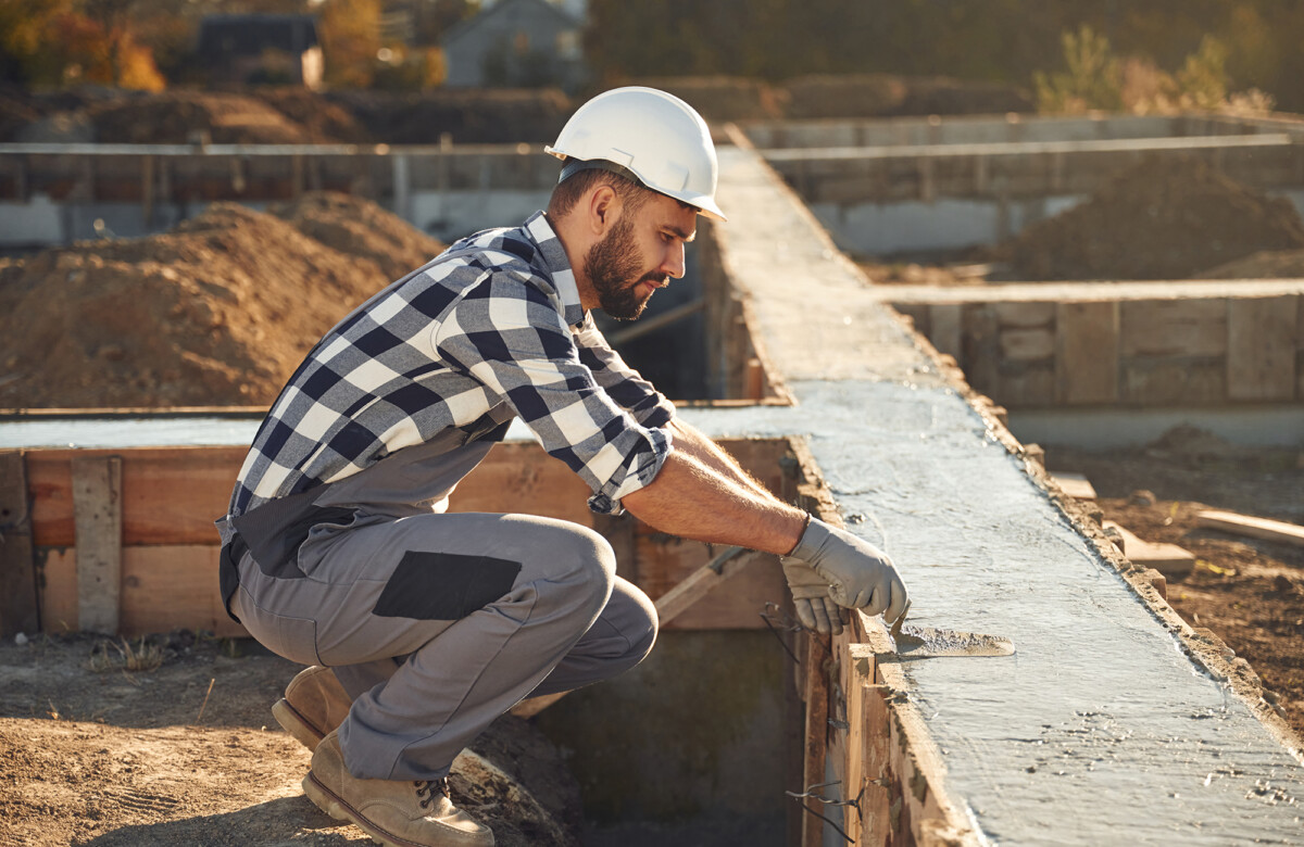 Sitting, working with foundation of the house. Man is on the construction site at daytime