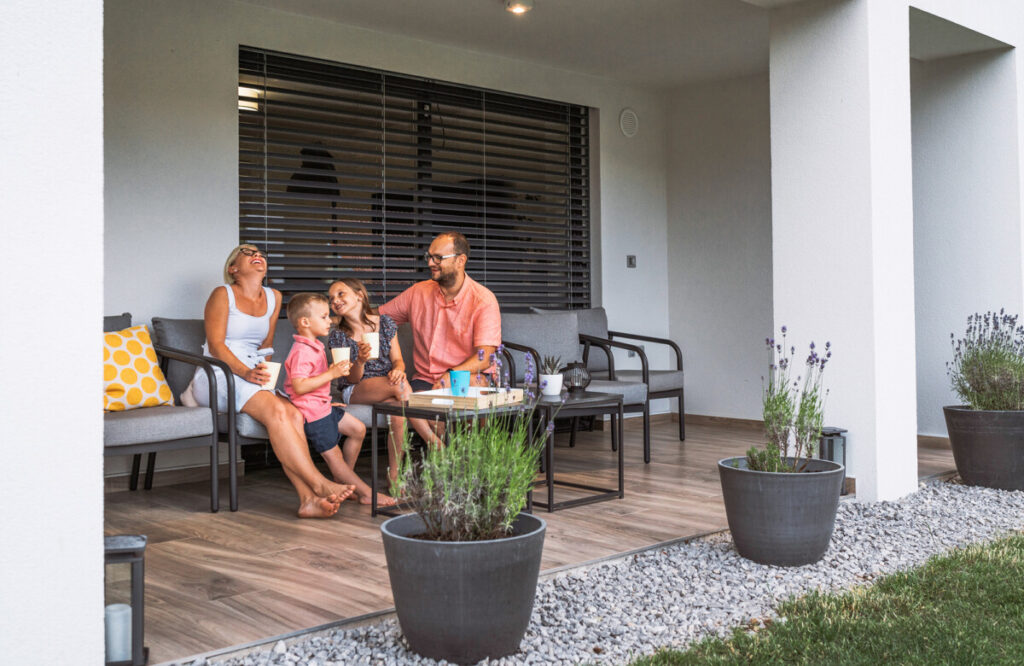 Family sitting outside their house on a nice terrace in the shade, having a drink on a hot summer day