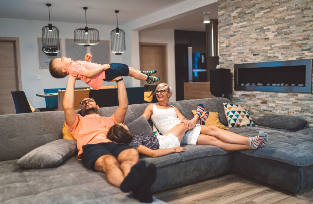 Family relaxing on the sofa while dad holds a young boy laughing up in the air